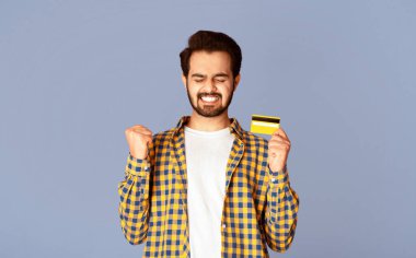 Heyecanlı Hintli adam kredi kartıyla mor arka planda EVET işareti yapıyor, panorama