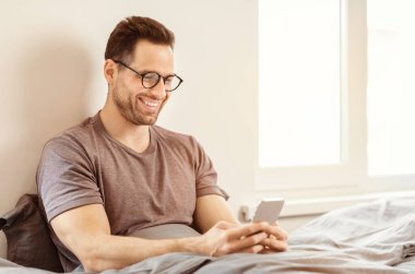 Gülümseyen Adam, hafta sonu sabahı evde yatakta oturan akıllı telefon uygulamasını kullanıyor. Metin için Boş Alan