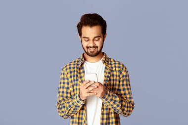 Pozitif Hintli adam cep telefonu ekranına bakıyor ve menekşe arkaplanda gülümsüyor.