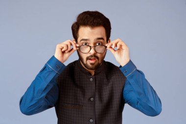 Çekici Hintli adam, eflatun arkaplanda şaşırarak gözlüklerini çıkarıyor.