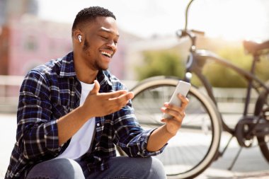 Modern İletişim. Neşeli, mutlu Afrikalı adam akıllı telefondan video görüşmesi yapıyor, arkadaşlarıyla konuşuyor ve el kol hareketi yapıyor.