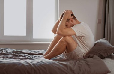 Mutsuz adam depresyon geçiriyor. Kafasına dokunuyor. Yatak odasında, yatak odasında oturan sorunları düşünüyor. Erkek Akıl Sağlığı Sorunu, Stres Konsepti. Metin için Boş Alan
