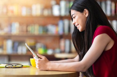 Kentteki kafede kahve molası sırasında akıllı telefon kullanan gülümseyen Asyalı kadın görüntüsü