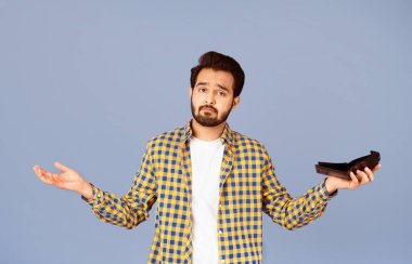 Ekonomik kriz ve iflas. Boş cüzdanı olan, omuzlarını mor arka planda silkeleyen üzgün Hintli adam.