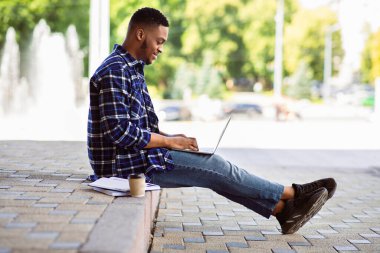 Dizüstü bilgisayarda çalışan Afrikalı bir adamın yan görünüşü. Sınırda oturuyor, seçici bir şekilde.