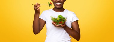 Sağlıklı gülümseyen siyah kız sarı stüdyo arka planında taze salata yiyor sağlıklı yemek ve diyet konsepti