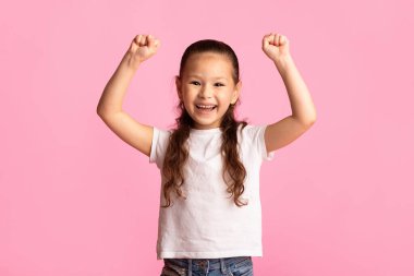 Yaşa! Heyecanlı Asyalı çocuk kazanan jestler yapıyor, yumruklarını kaldırıyor, pastel pembe stüdyo duvarına izole edilmiş, uzay kopyaları yapıyor.