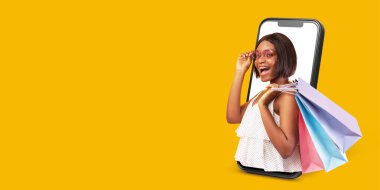 Memnun bir müşteri akıllı telefon kullanarak online alışveriş yapıyor. Elinde alışveriş torbaları ve tebessümlerle dijital ticaretin rahatlığını ve neşesini parlak sarı bir arka planda sergiliyor..