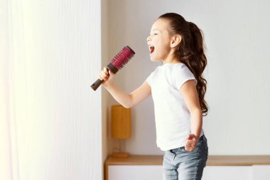Asyalı Kız Şarkı Söylüyor Saç fırçasıyla eğleniyor Evde koltukta zıplıyor. Hafta sonu konsepti. Boşluğu Kopyala