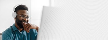 Genç bir Afrikalı Amerikalı adam modern bir ofiste işine odaklanmış durumda. Kulaklık takıyor, görevlerini yaparken gülümsüyor, olumlu bir girişimci yaşam tarzını yansıtıyor, alanı kopyalıyor.