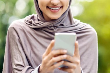 Güzel gülümseyen Arap kız tesettürde modern akıllı telefonu kullanıyor, parkta tek başına vakit geçiriyor, kopyalama alanı, yakın çekim