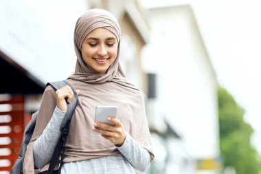 Sırt çantalı pozitif müslüman kız şehrin yanından geçerken akıllı telefon kullanıyor, boşluğu kopyala