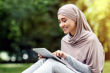 Genç Müslüman kadın parkta dinlenirken dijital tablet kullanıyor.