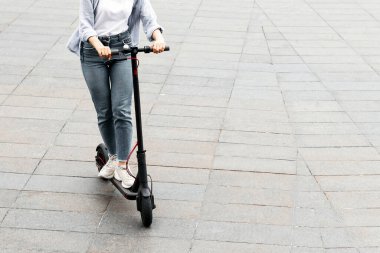 Tuğla yolda siyah e-scooter kullanan sıradan bir kızın yüksek açılı portresi, reklam veya metin için boş alan