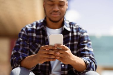 Teknoloji Konsepti. Cep telefonu kullanan, açık havada oturan, cihaza odaklanmış afro kişinin yakın plan portresi.