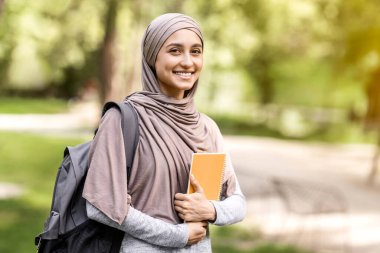 Sırt çantalı, elinde kitaplarla üniversiteden sonra parkta yürüyen güzel, gülümseyen Arap kız.