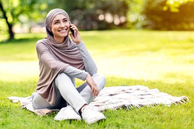 Rahat Arap kız parkta çimlerde oturuyor ve telefonla konuşuyor, boşluğu kopyalıyor.