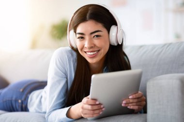 Boş Zaman Teknolojileri. Dijital tabletli ve kablosuz kulaklıklı gülümseyen Koreli kızın portresi.