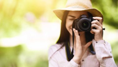 Fotoğrafçılık aşığı. Genç Asyalı kadın modern kamerayla dışarıda çekim yapıyor, objeye odaklanıyor, fotoğraf çekmekten zevk alıyor, mekanı kopyalıyor.