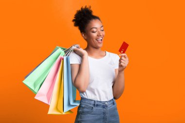 İnternetten Alışveriş Konsepti. Sarı stüdyo duvarında kredi kartı ve kese kâğıdı tutan heyecanlı zenci kadın.