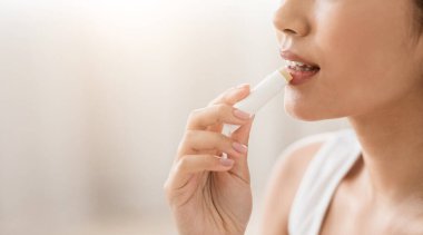 Genç Asyalı kadın ruj kullanıyor, yatak odasının içi boş. Tanınamayacak bir kadının güzel dudaklarıyla ilgilenmesi, eve hijyenik ruj sürmesi, yakın çekim...