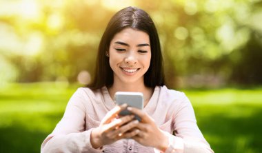 Neşeli Asyalı kız dışarıda akıllı telefondan mesaj atıyor, Yeşil Park 'ta dinlenirken arkadaşlarıyla sohbet ediyor,