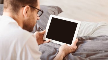 Evdeki yatak odasında yatağında uzanan, boş ekranlı dijital tablet kullanan bir adam. Uygulama ve Web sitesi Reklam Kavramı için Bilgisayar Boş Görünümü. Panorama, Mockup
