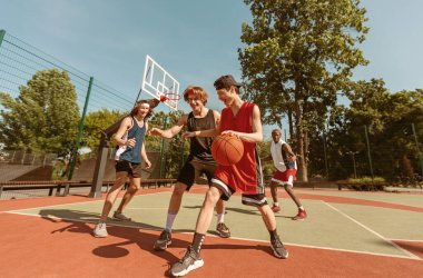 Bir grup genç basketbolcu oyunlarını açık hava spor sahasında oynuyorlar.