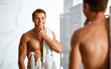 Yakışıklı adam elleriyle çenesine dokunuyor ve aynadan kameraya bakıyor.