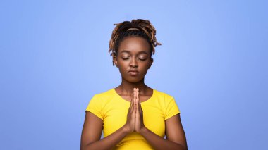 Genç siyahi kadın yalvarma jestinde sıkıca sarılmış ellerini gösteriyor, lütfen mor stüdyo arka planında, kopyalama alanı. Dini bütün bir Afrikalı kadın daha iyi bir gelecek umuduyla gözleri kapalı dua ediyor.