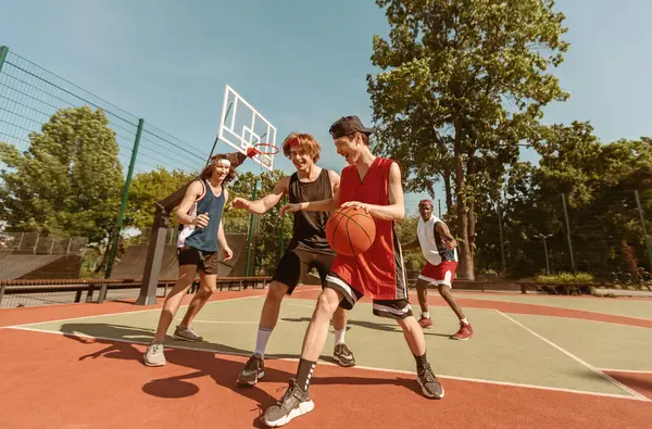 Bir grup genç basketbolcu oyunlarını açık hava spor sahasında oynuyorlar.