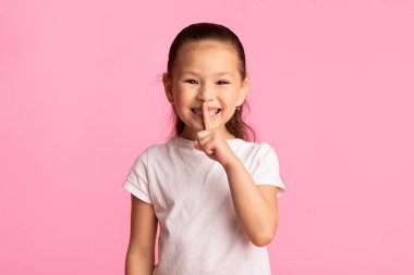 Sessizlik Konsepti 'ni koru. Neşeli Asyalı çocuk parmağını dudaklarına koyuyor, kopyalama alanı, pastel pembe stüdyo duvarı