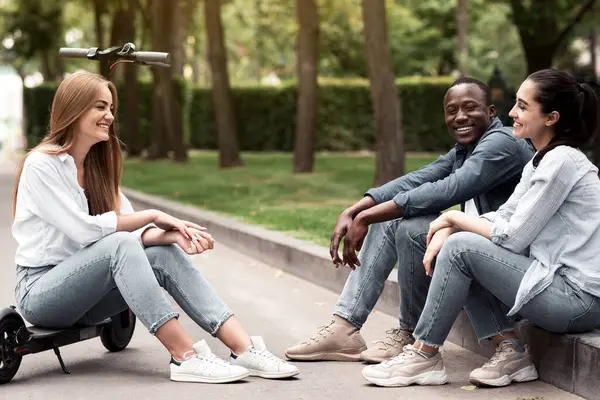 Üç farklı genç bir şehir parkında toplanıyor, biri scooter 'da dinlenirken gülüyorlar. Açık hava manzarası, öğleden sonra güneşinin genç ve canlı bir anını yakalıyor..