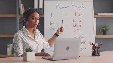 Genç bir Afrikalı Amerikalı kadın internette İngilizce öğretiyor, öğrencilerini açık açıklamalarla meşgul ediyor. Dersini geliştirmek için beyaz tahta ve akıllı telefon kamerası kullanıyor..