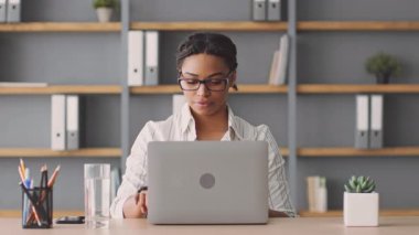 Kendini işine adamış bir Afrikalı Amerikalı kadın internet üzerinden özel ders veriyor. Kitap rafları ve çalışma materyalleriyle çevrili bir masada otururken dizüstü bilgisayar kullanıyor..