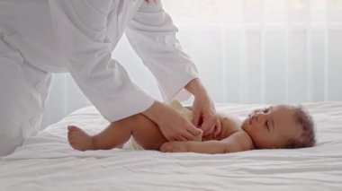 Bakıcı, bebeğin yumuşak bir yatakta rahat etmesini sağlamak için bebeğin bezini içeride nazikçe değiştirir. Doğal ışık odayı dolduruyor, özel bakım anını vurguluyor..