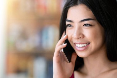 Telefon var. Kapalı alanda cep telefonuyla konuşan güzel Asyalı kızın yakın plan portresi, kopyalama alanı ile seçmeli odak
