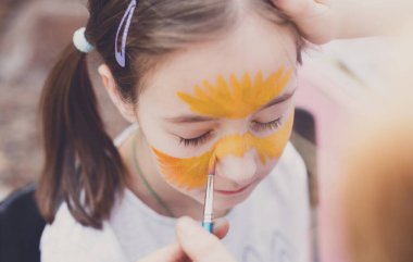 Çocuk animasyoncusu, ressamlar küçük kıza yüz resmi çizer. Komik yüzlü çocuk. Ressam kızların yüzüne kaplan gibi bakıyor. Çocuklar tatil, etkinlik, doğum günü partisi, eğlence.