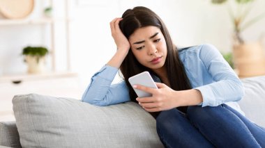 Evde Sıkıldım. Oturma odasında akıllı telefonuyla oturan yorgun Asyalı kız.