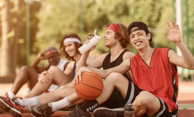 Asyalı oyuncu ve çok uluslu takımı basketbol sahasında dinleniyorlar, boş alan. Panorama