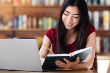 Çalışma Planı Shedule. Asyalı Kız Kafe 'de dizüstü bilgisayarda çalışıyor ve Not Defteri' ne notlar yazıyor.