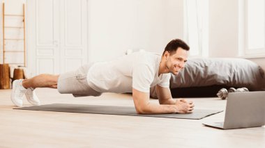 Evde eğitim. Çevrimiçi antreman sırasında dizüstü bilgisayarda egzersiz yapan adam. Panorama