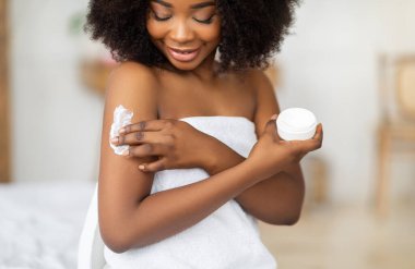 Güzel siyah bayan banyo üstüne havlu giyiyor, krem sürüyor, evde vücut yağını besliyor. Güzel Afrikalı Amerikalı kadın cildini nemlendiriyor, kaplıca ameliyatından zevk alıyor.