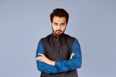 Eflatun arka planda çapraz kollu ciddi Hintli bir adamın portresi.