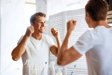 Diş bakımı. Diş ipi kullanan yakışıklı bir adamın portresi aynaya bakıyor, omzunun üstünden bakıyor.