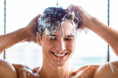 Mutlu gülümseyen genç bir adamın portresi duş alan, evdeki banyoda sıcak suyun altında duran. Erkek Saç Bakımı Kozmetik ve Hijyen Rutin Konsepti