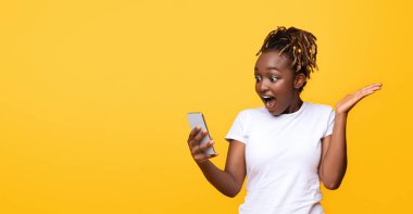 İnternette inanılmaz satışlar. Şaşkın siyah kız cep telefonuna bakıyor, sarı arka plan, panorama