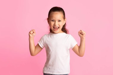 Kazan Kavramı. Heyecanlı Asyalı çocuk portresi, ellerini kaldırıp pembe arka planda yumruklarını sallıyor.