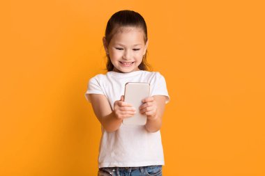 Akıllı telefon kullanan, gülümseyen, pastel sarı duvarın üzerinde duran tatlı Asyalı çocuk.