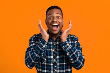 Heyecanlı siyah adam heyecanla el ele tutuşarak bağırıyor. Stüdyoda sarı arka planda poz veriyor. Sürpriz, Omg Kavramı